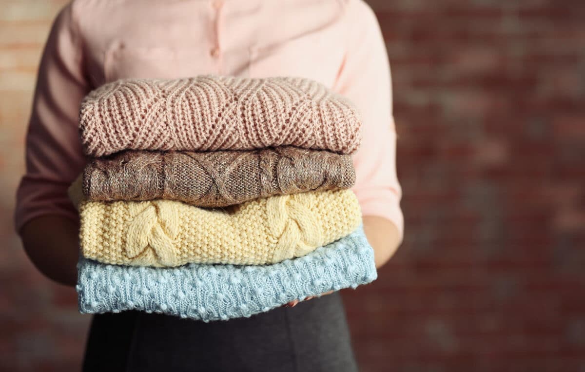 Choix de lessive avisé : une femme tenant des pulls fragiles, soulignant que la lessive à la cendre n'est pas toujours la meilleure option pour certains textiles