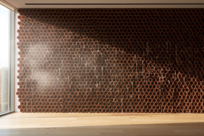 Mur intérieur tapissé de cônes en terre cuite empilés en ruche, ruisselant d'eau dans une pièce lumineuse.