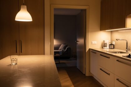 Cuisine et salon d'un appartement la nuit, plan de travail essuyé et plaid plié sur le canapé sous une lumière de lampe douce.