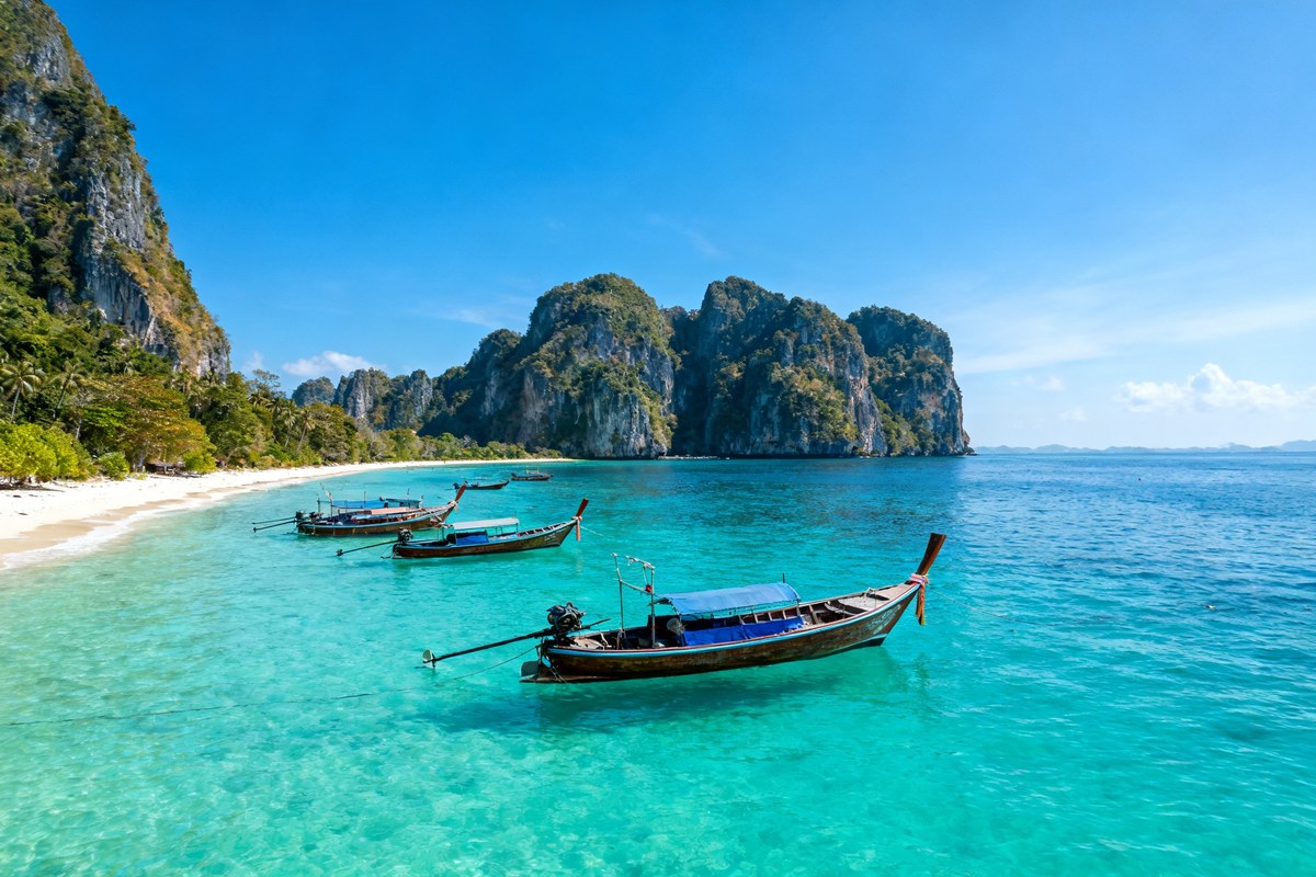 Plage tropicale de Thaïlande avec bateaux longtail, eau turquoise et falaises calcaires