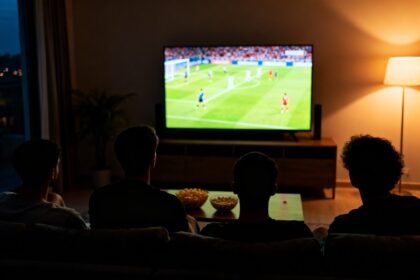 Amis vus de dos sur un canapé, regardant un match de football à la télévision dans un salon faiblement éclairé