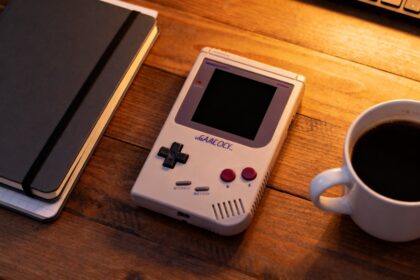 Console de jeu portable rétro posée sur un bureau en bois avec un carnet et un café