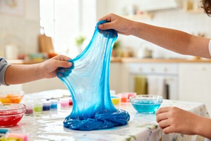 Mains d'enfants étirant un slime bleu brillant sur une table couverte de fournitures créatives