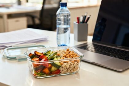 Lunchbox en verre ouverte sur un bureau, garnie de céréales, légumes rôtis et pois chiches