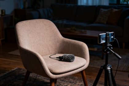 Un fauteuil beige vide face à un smartphone sur trépied, un micro posé sur l'assise, dans un salon en lumière tamisée.