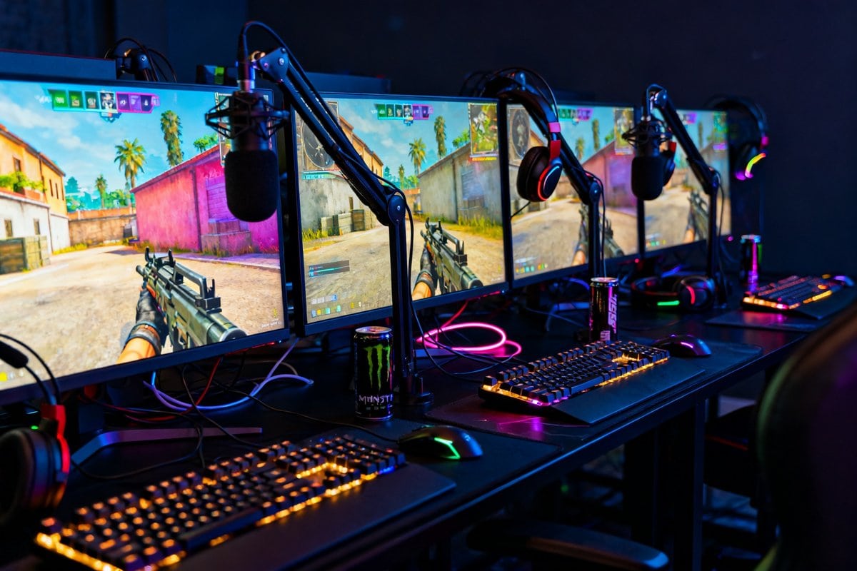 Salle de jeu plongée dans la pénombre avec quatre postes de streaming et écrans allumés sur un jeu de tir