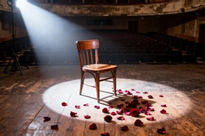 Chaise en bois vide sous un projecteur sur la scène d'un vieux théâtre, pétales de roses rouges au sol