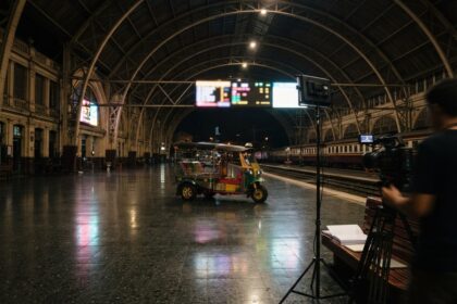 Tuk-tuk coloré au centre du hall voûté d'une gare la nuit, près d'une caméra de tournage